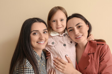 Young lesbian couple with adopted little girl on beige background, closeup