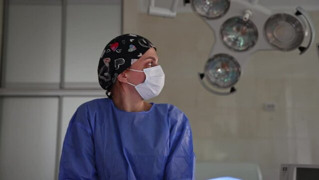Female doctor assisting at operation looks at the monitor. Medic in black cap and mask working in surgery room.