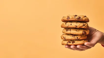 Foto op Plexiglas Hand holding chocolate chip cookies isolated on orange background, copyspace for text, American cookie © Mrt
