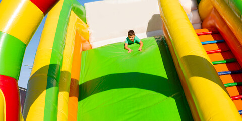 Fototapeta na wymiar Little boy child ride upside down on an inflatable multi-colored slide. Sliding head down 