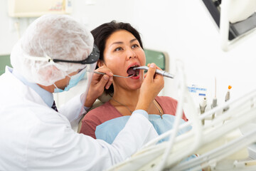 Professional dentist filling teeth for woman patient sitting in medical chair