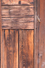 The side of a redwood house has vertical and horizontal planks with nails sticking out. A blue...