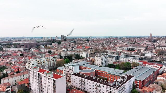 Aerial of Montpellier's Beaux Arts: urban charm with seagulls soaring under cloudy skies.




