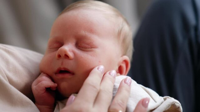 Adorable newborn sleeping tight in mother's hands. Mom's hand strokes tender baby cheek. Close up.