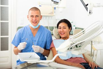 Portrait of a smiling man dentist with a positive woman patient sitting in a dental chair in the clinic office