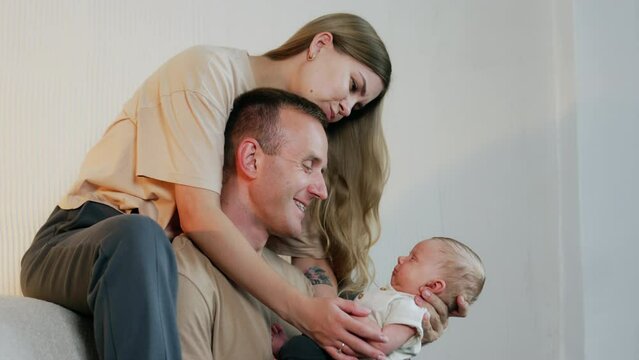 Lovely newborn baby in dad's arms looks at his parents. Smiling couple making faces to a kid.