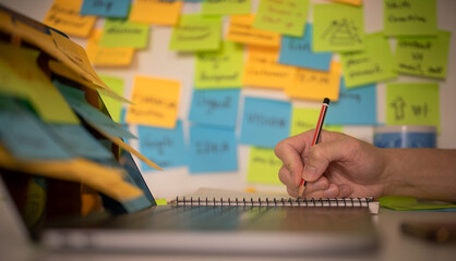 blurred colorful post note background, man using pencil and computer laptop working on memo note memorandum in office, reminder messages for working schedule, things to do list