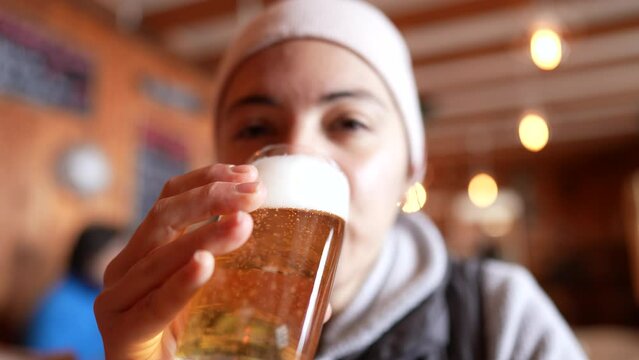 Woman drinking draft beer at restaurant during cold season. Close-up face of person drinks refreshing alcoholic beverage
