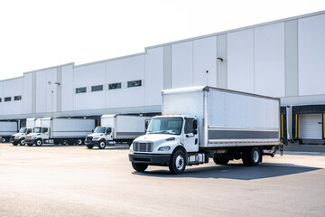 Huge warehouse building with docks and gates and loading cargo middle duty day cab rigs semi trucks...