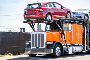 Orange car hauler big rig classic semi truck tractor with loaded hydraulic semi trailer standing on...