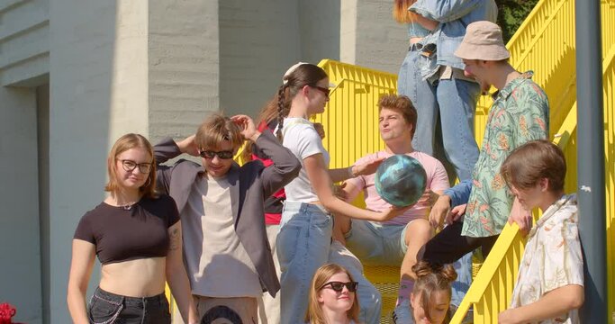 Students talking during a study break, girl with ball. Yellow staircase in urban environment, outdoor lifestyle social gathering, building relationships. Chat informally, catch up with friends. 
