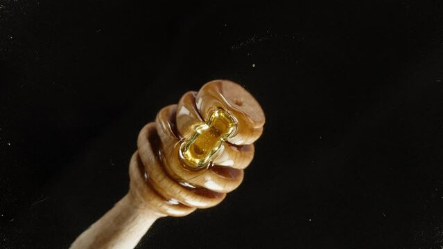 Dipping a wooden honey spoon into honey, viewed from below through glass, close-up shot against a black background.
