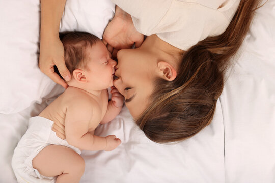 Mother kissing her cute newborn baby on bed, top view