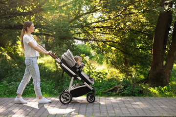 Fototapeta na wymiar Happy nanny with baby in stroller walking in park, space for text