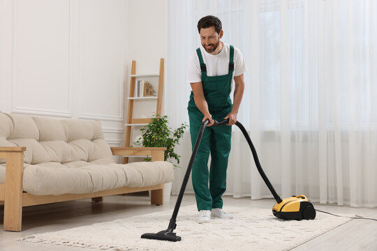 Dry cleaner's employee hoovering carpet with vacuum cleaner in room