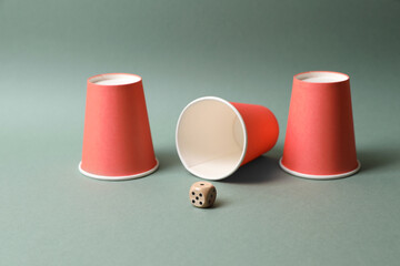 Three red cups and dice on pale olive background. Thimblerig game