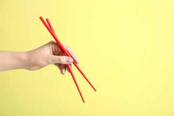 Woman holding pair of red chopsticks on yellow background, closeup. Space for text