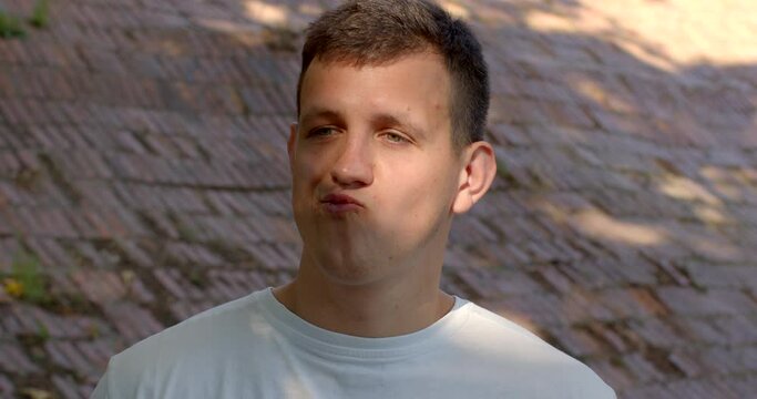 Young man gazes into the camera nodding in agreement. Close-up male portrait outside. Non-verbal gesture signifies that he is in accord with something being said or suggested. Non-Verbal Communication