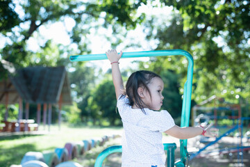 Fototapeta premium Asian girl playing on the playground with a trapeze Enthusiastic child hanging on the bar with two hands Children exercising.