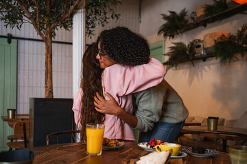 Two female friends hugging each other after long time no see. They are in a coffee shop for brunch
