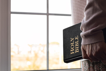 Woman standing near window holding Bible