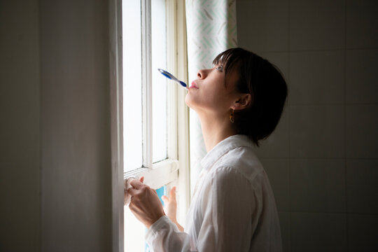 歯ブラシをくわえながら窓を開けている女性