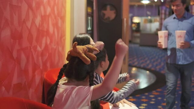 Cheerful Asian family at cinema show. Mum and kids sit in theater seat, waiting for father's popcorn before watching movie, and happy together, a public indoor entertainment lifestyle with film shows.