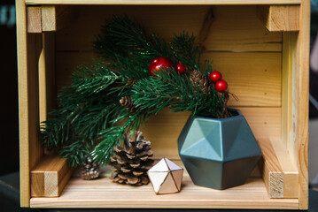 Christmas decoration in the form of a Christmas tree branch on a wooden shelf with geometric figure and a pine cone