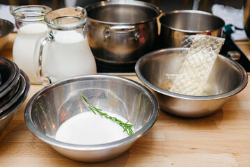 set of products for preparing panna cotta dessert: dry gelatin sheet, sugar, jugs of milk and cream, stainless steel bowls and pans