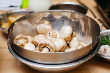 Fresh champignon mushrooms in a metal bowl on a wooden table, raw food ready to cook