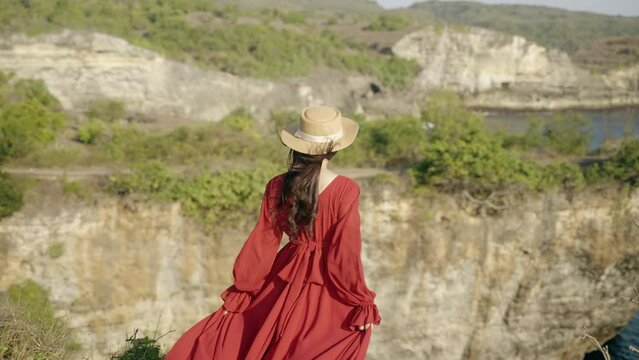 Nusa penida island, Bali, indonesia. 4K video Young woman red dress stand relaxing at viewpoint broken beach, beutiful broken beach,Nusa Penida island. Popular travel destination on Bali, indonesia.