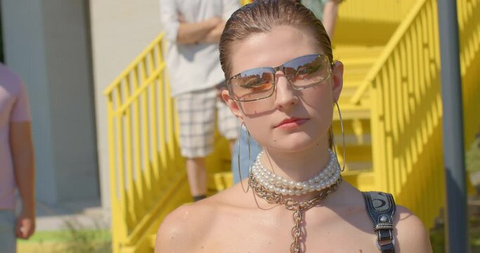 Zoomers portrait of young woman wearing sunglasses looking into camera, posing. Personal casual style elements of current fashion trends. Yellow urban background. Generation Z. Diverse and Inclusive