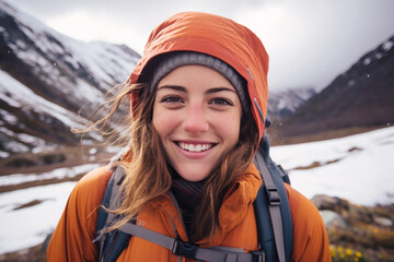 Fototapeta na wymiar Young woman smiling in jacket and backpack hiking up snowy mountain