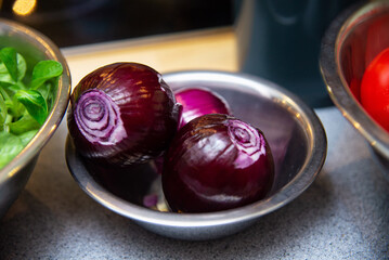 Fresh red onions in metal bowl on kitchen table. Selective focus.
