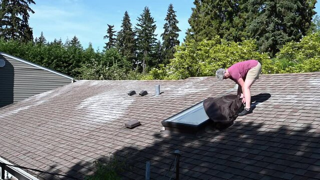 Middle aged woman installing a skylight cover over a rectangular skylight on a roof in the spring
