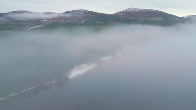 Descending through the thick mist to reveal campers on snow covered lakeside