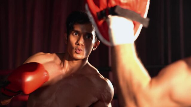 Asian and Caucasian Muay Thai boxer unleash punch in fierce boxing training session, delivering punching strike to sparring trainer, showcasing Muay Thai boxing technique and skill. Impetus