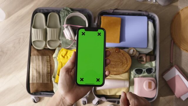 Green screen phone packed suitcase. Woman hold phone checking luggage, list of necessary things for trip. Focused serious preparation for long trip vacation checking baggage before leaving for airport