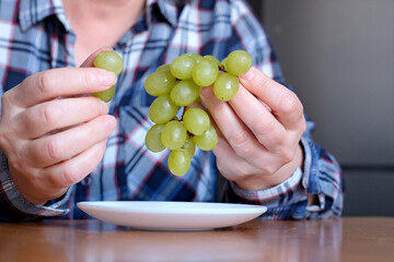 The hands of an elderly woman holds a small brush of white seedless grapes