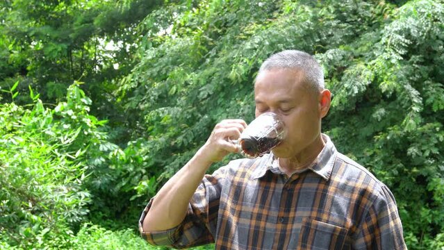 Middle-aged Asian man happily drinking cola water placed in a transparent glass on a sunny summer day. Drinking cool soda can help you cool down. Summer drink concept