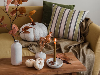 Autumn interior of the living room - sofa with pillows and blankets, wooden bench with autumn decor