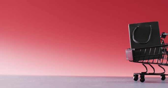 Video of black gift bag in shopping trolley with copy space on red background