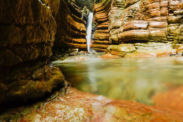 small waterfall and flowing water in the red canyon with layers of red rocks in austria