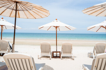 Beach in Thailand. White umbrellas and deck chairs on the sand against the sea.