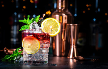 Bramble cocktail drink with dry gin, liqueur, syrup, lemon juice, blackberry, mint and ice. Black...