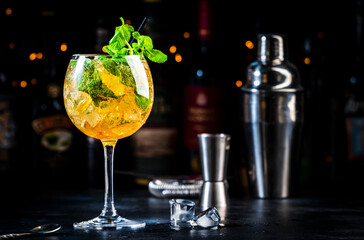 Spring melody cocktail drink with cognac, liqueur, prosecco or sparkling wine with ice and fresh mint in wine glass, dark background, bar tools and bottles
