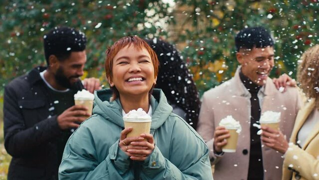Group of young friends wearing winter coats standing outside in snow holding takeaway hot chocolate drinks - shot in slow motion