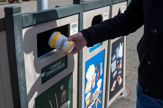 Vancouver, BC, Canada - 5 April 2023. Male hand throws away Yellow cup of Blenz Coffee to the rubbish bin