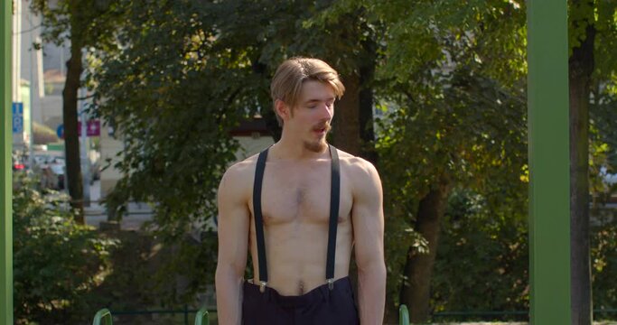 Young man posing at urban workout area with pull-up bars, preparing to do physical exercises. Guy sporty and healthy physique, shirtless male portrait. Sunny outdoors. Fitness people lifestyle