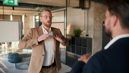 Close-up shot of two male office workers practicing breathing techniques during a break between work. A blond man in a brown jacket and a white shirt and a brunette man in a blue jacket doing